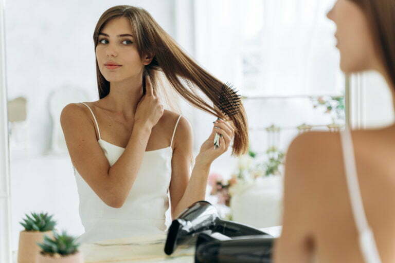 Portrait of the woman reflected in mirror doing daily routine while holding hairbrush tidy her hair