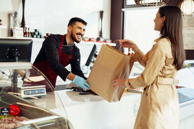 Shop assistant handling shopping bag to female customer in grocery store